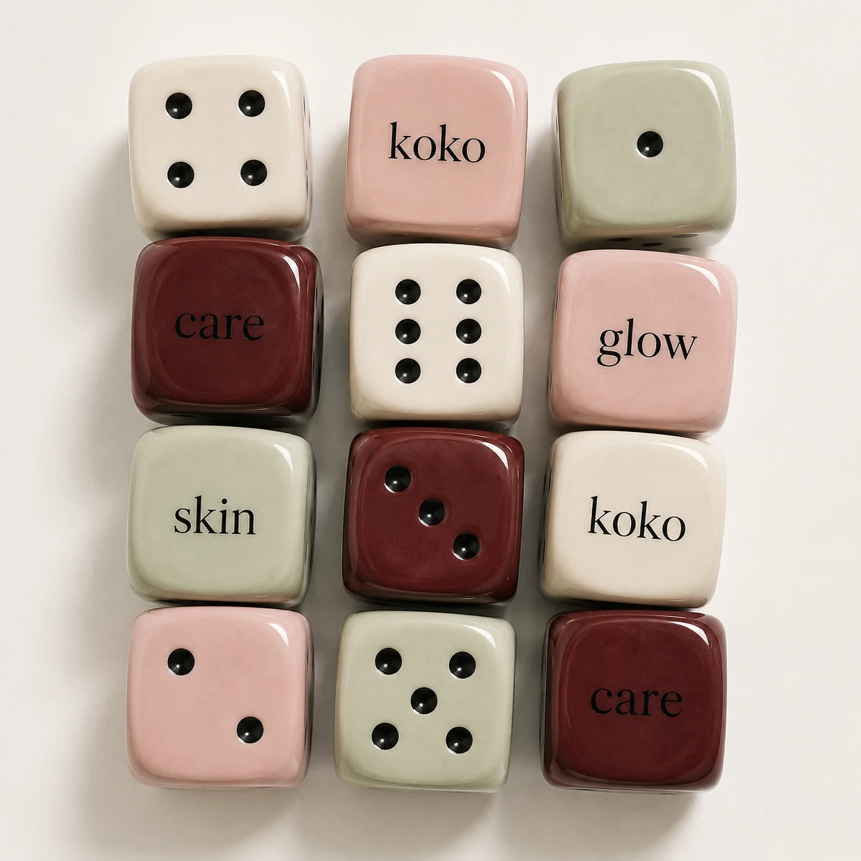Glossy Koko cubes in pink, burgundy, sage and white, with dice dots and the words care, glow and skin