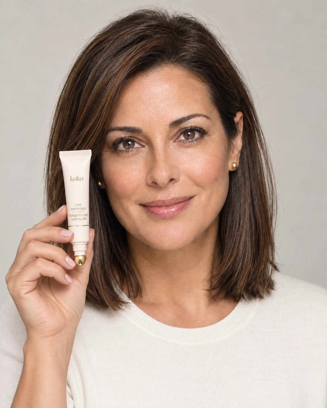 Brunette woman with polished makeup holding Koko Line Erase Primer